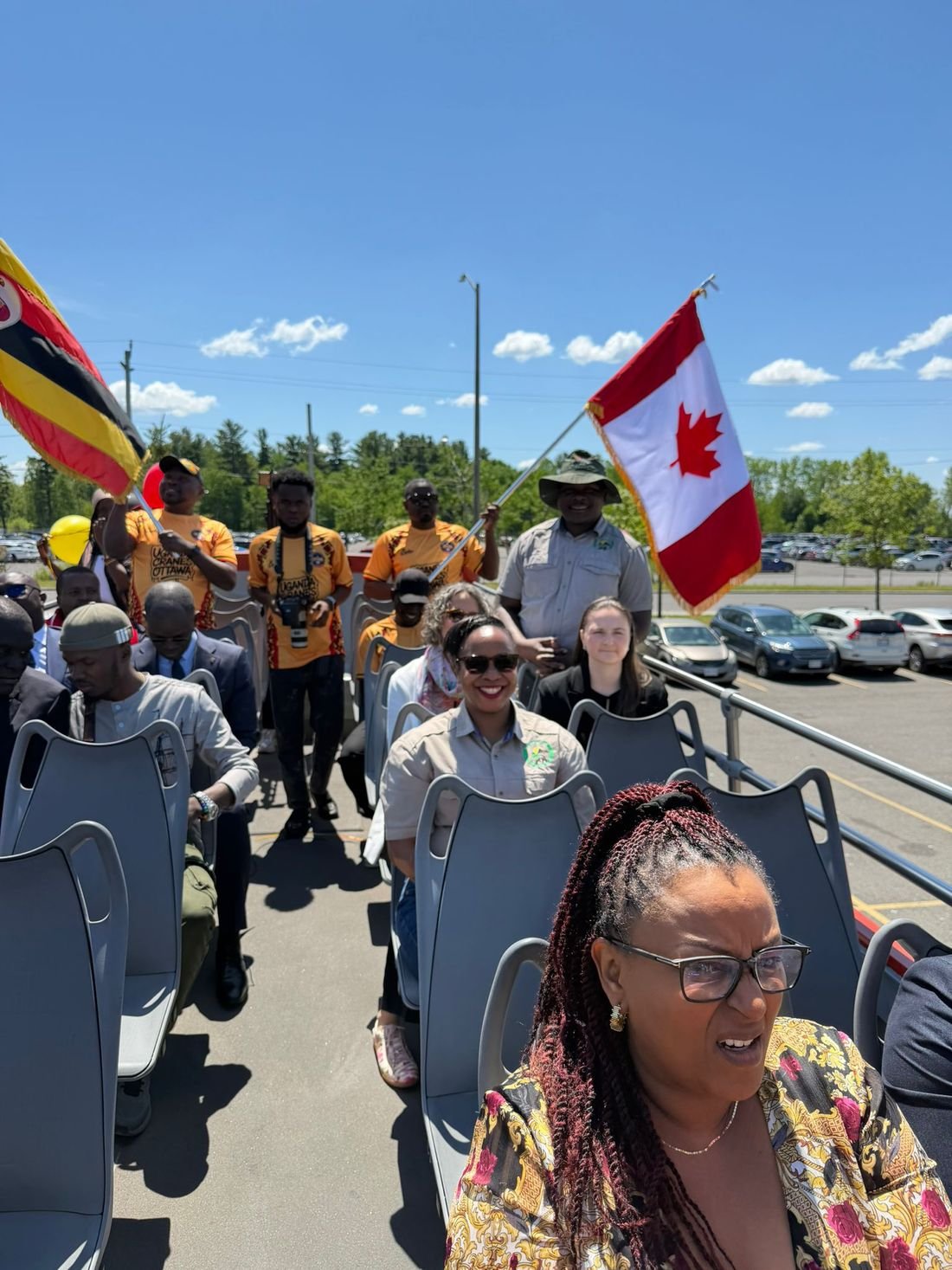 Bashem travellers and community members on an open-top bus at a Ugandan community event in Ottawa, with Ugandan and Canadian flags