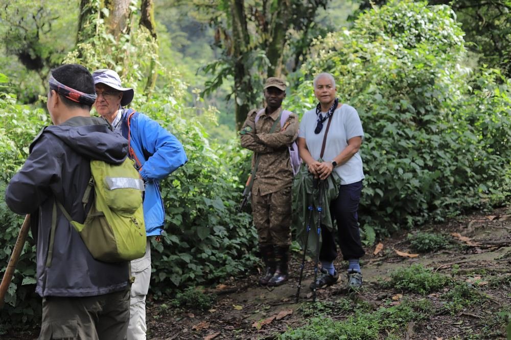 Four travellers and an armed Uganda Wildlife Authority ranger on a wet forest trail inside Bwindi